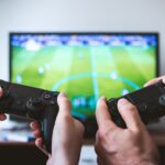 two people holding black gaming consoles